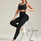 Woman in black ribbed sports bra and high-waisted leggings with white sneakers, seated on chrome chair