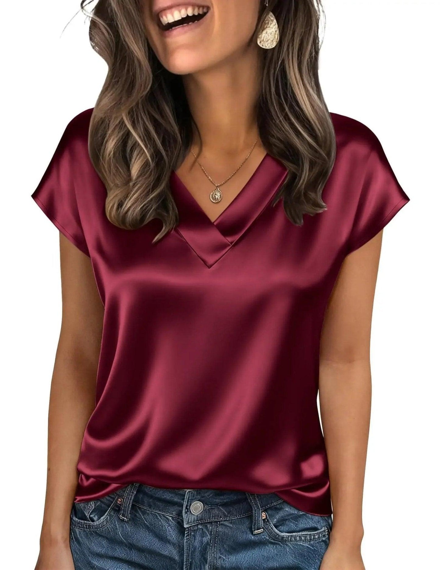 Woman wearing burgundy satin V-neck top with short sleeves, paired with jeans, gold necklace and earrings