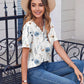 Woman in floral print blouse, straw hat, and jeans sitting on bench